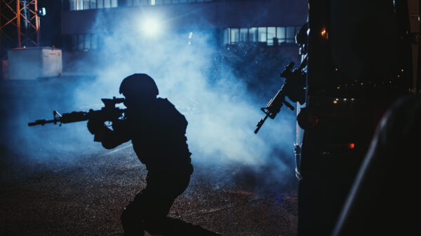 Silhouette Of Team Of Armed soldiersExit A Black Van Parked Outside Of An Office Building. Soldiers With Rifles And Flashlights Run On A Street Filled With Smoke