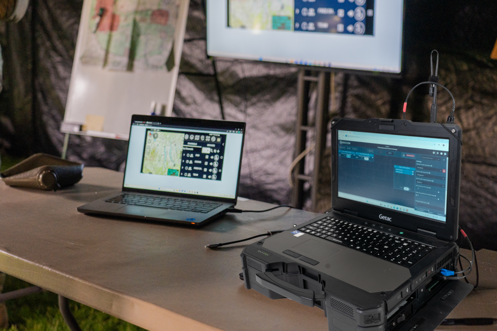REDCOM STRIKE on a table in a TOC. REDCOM Sigma C2 Console is on the STRIKE console which is on a Getac tactical laptop.
